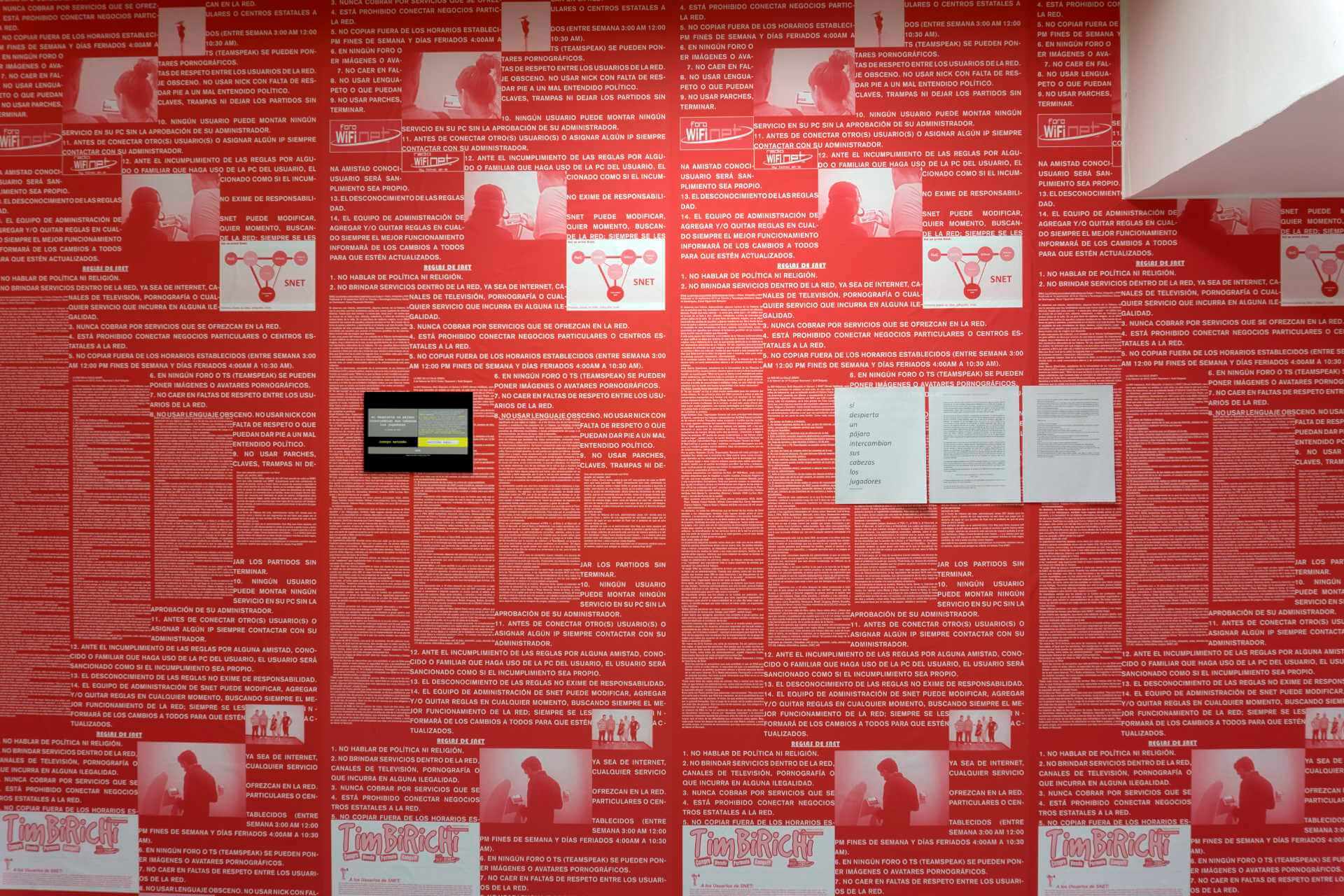 A wall with red paper wall with messages of a poem by Ernesto Oroza for SNET called Si despierta un pájaro intercambian sus cabezas los jugadores