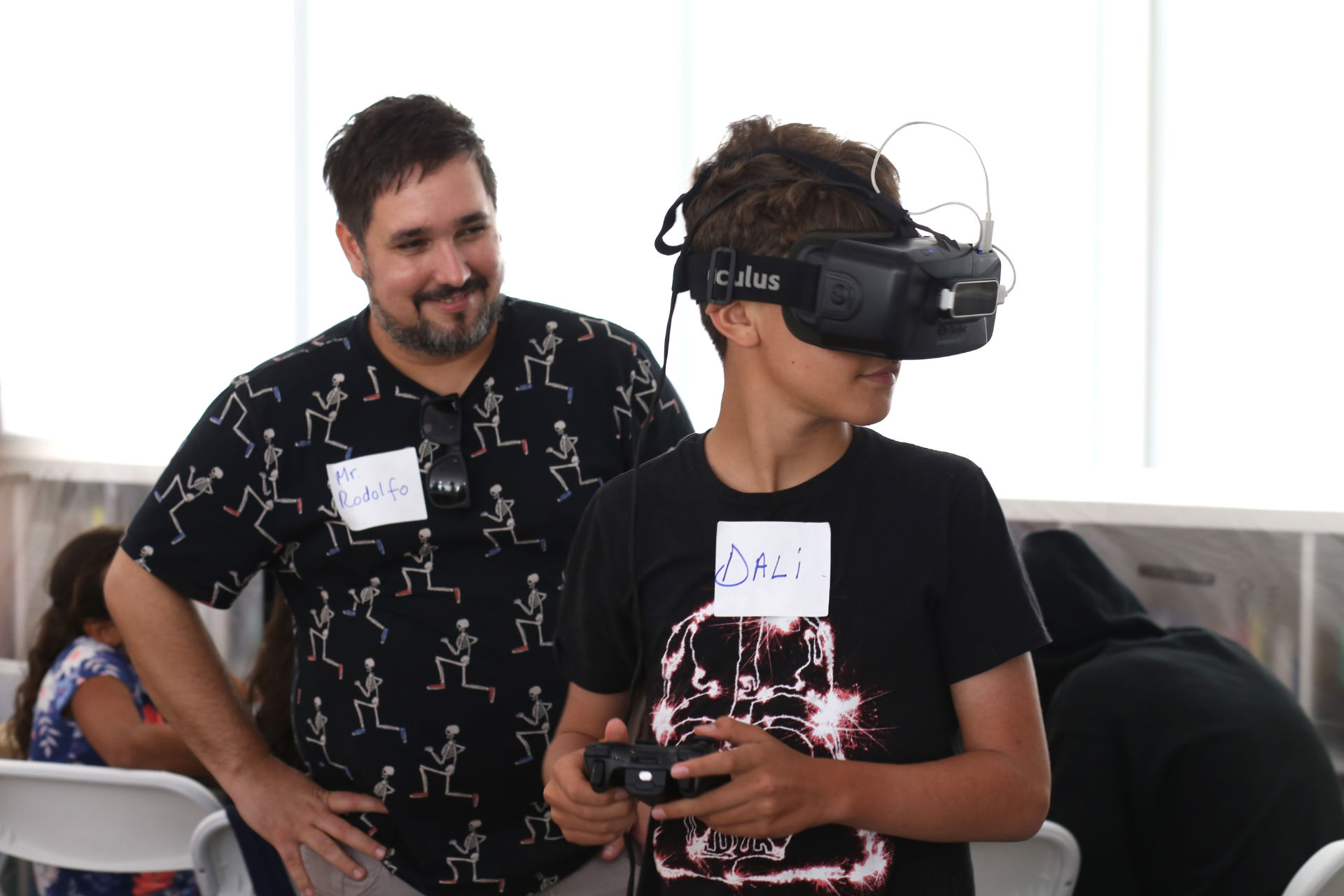 A boy using an Oculus and playing, and a Man smiling behind him
